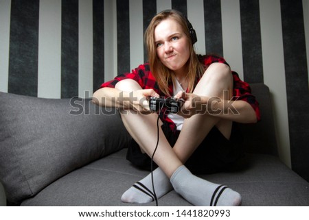 young cheerful girl sits on the couch and plays the console on the joystick, she is focused on video games