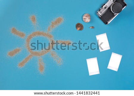 Photo frame and camera with photos on blue background . Sun drawn by the sand on blue background. Top view.