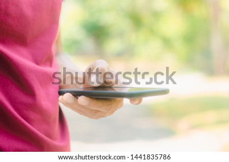 close up handsome man use hand typing mobile phones and touch screen working search with app devices in park with sunrise and green blur nature background.