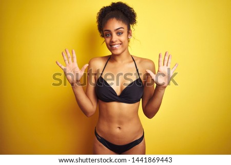 African american woman on vacation wearing bikini standing over isolated yellow background showing and pointing up with fingers number ten while smiling confident and happy.