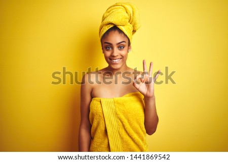 Young african american woman wearing towel after shower over isolated yellow background doing ok sign with fingers, excellent symbol