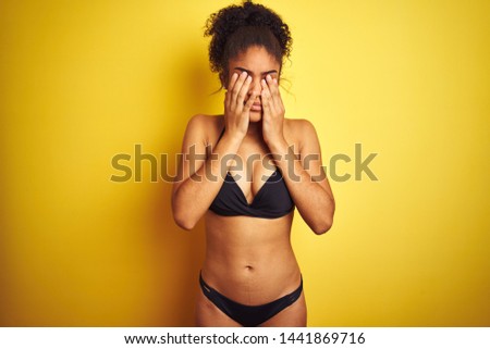 African american woman on vacation wearing bikini standing over isolated yellow background rubbing eyes for fatigue and headache, sleepy and tired expression. Vision problem