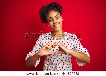 African american woman wearing fashion white dress standing over isolated red background smiling in love doing heart symbol shape with hands. Romantic concept.