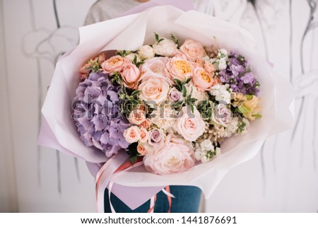 Very nice young woman holding big and beautiful bouquet of fresh hydrangea, roses, carnations, eustoma, matthiola in purple and peach colors, cropped photo, bouquet close up