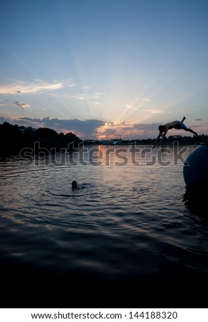 silhouette of man jumping in lake at sunset 