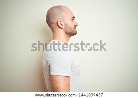 Young bald man with beard wearing casual white t-shirt over isolated background looking to side, relax profile pose with natural face with confident smile.