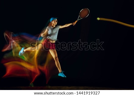 One caucasian woman playing tennis isolated on black background in mixed and stobe light. Fit young female player in motion or action during sport game. Concept of movement, sport, healthy lifestyle.