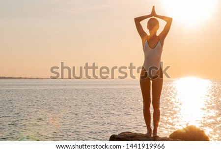 Silhouette woman yoga on the beach at sunset. Woman is practicing yoga at sunrise on sea shore. Calm and self control.