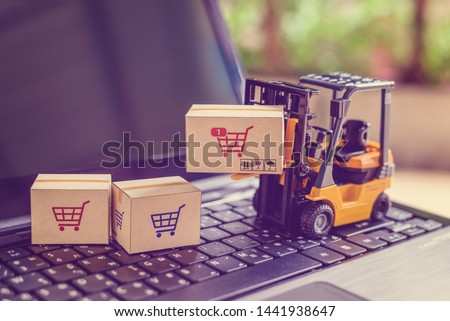 Logistics and supply chain management for online shopping concept : Fork-lift moves a box with a red shopping cart logo, 2 cartons on a laptop computer, depicts delivering goods or products in a store Royalty-Free Stock Photo #1441938647