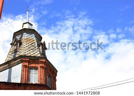 The sky with white clouds and a view of the roof of the house view below. The house is made of brown brick. Summer morning time. The effect of sunlight
