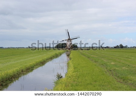 Beautiful view over a meadow with a traditional and characteristic Dutch water windmill against a beautiful blue sky with white clouds.