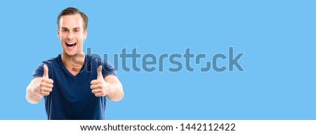Portrait of happy smiling man in blue casual clothing, showing thumb up gesture, against blue color background. Male caucasian model at studio. Copyspace area for some ad sign text.