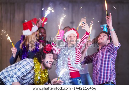 multiethnic group of young happy casual business people taking selfie picture while dancing with sparklers and having fun during new year party in front of concrete wall at new startup office