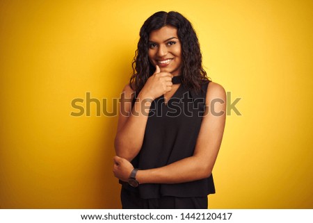Transsexual transgender elegant businesswoman standing over isolated yellow background looking confident at the camera smiling with crossed arms and hand raised on chin. Thinking positive.