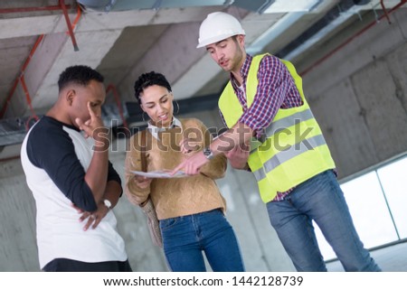 architect engineer using tablet computer while showing house design plans to a young multiethnic couple at construction site