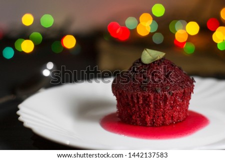 Red cupcake with chocolate chips on a dark background with multi-colored bokeh