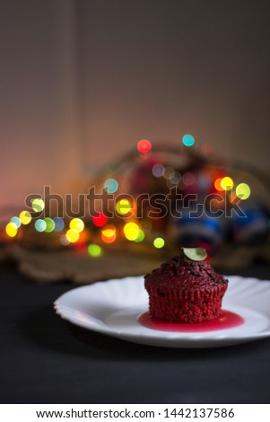 Red cupcake with chocolate chips on a dark background with multi-colored bokeh