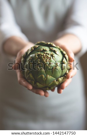 The girl is holding an artichoke with a blurred background, the concept of proper and dietary nutrition, dottex. Vertical picture