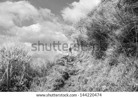 Mountaineer man walk on path of mountain under dramatic clouds, Infrared photography.