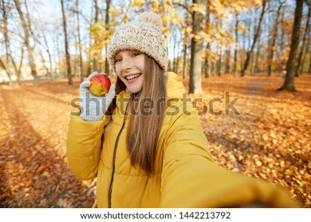 season and people concept - happy girl with apple taking selfie at autumn park
