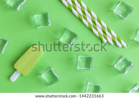 Flat lay of drinking straws, ice cubes and ice cream on green background minimal summer refreshment creative concept.