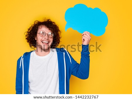 Funny young man in nerdy glasses smiling and holding empty thought balloon against yellow background