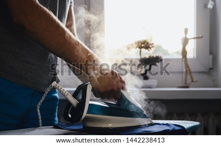 Man is ironing clothes. The concept of caring for the home, helping men in household chores. The man uses an iron to iron the child's clothes. Royalty-Free Stock Photo #1442238413
