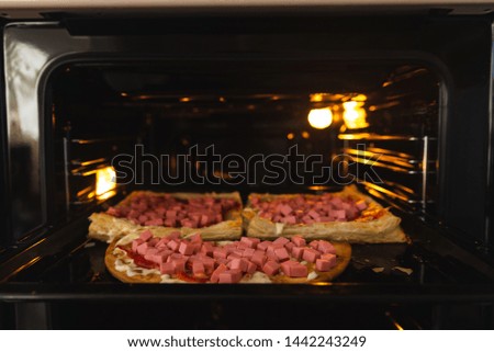 Homemade pizza in the oven close-up, sausage sprinkled with cheese