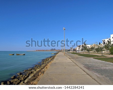 Panoramic view on seaside street near sea port Bushehr: waters of Persian gulf, walking side, stone bank, motor boats, & sea cargo containers (on background). Picture taken on west of Bushehr, Iran