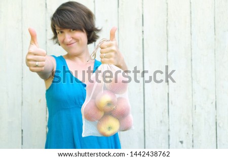 Zero waste shopping concept. No single use plastic. Woman holding reusable recycled mesh produce bag with apples and showing sign Like by hands. 