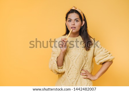 Beautiful young brunette woman in yellow clothes with thoughtful face hold pen, prepare to exam isolated on yellow wall background, studio portrait. People lifestyle concept. Royalty-Free Stock Photo #1442482007