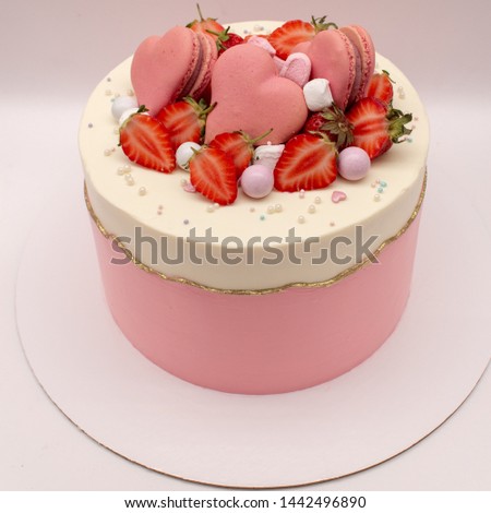 Delicate pink cake decorated with strawberries and heart-shaped macaroons. On a white background.