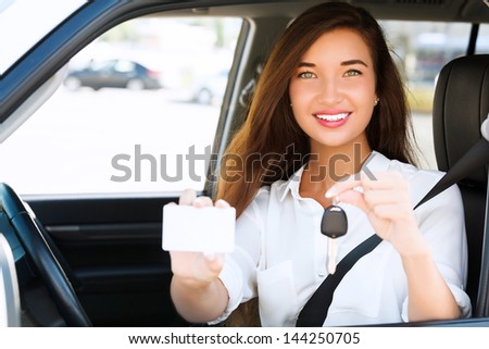 Happy girl in a car showing a key and an empty white card for your message