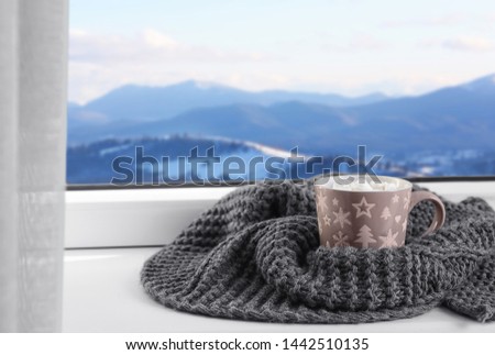 Hot drink and warm scarf near window with view of winter mountain landscape