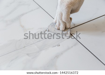 Grouting tiles seams with a rubber trowel. Royalty-Free Stock Photo #1442516372
