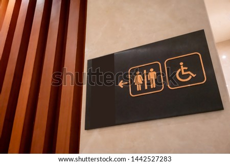 Restroom sign made of gold metal on black board hanging on white wall