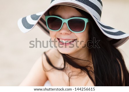 Happy young brunette girl pose outdoor in sun hat,sunglasses.Cute young brunette woman smiling.Toothy smile,summer beach outfit.Beautiful young girl enjoy summer vacation on beach.Happy girl portrait