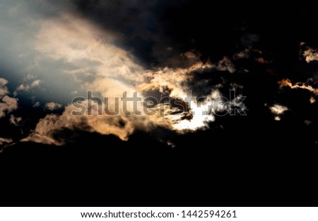 The Dark gray dramatic sky with sunlight through large clouds in rainy seasons.