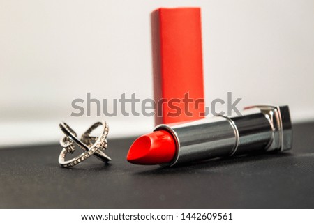 A red lipstick and a silver ring on the black and white background. Close up photo.