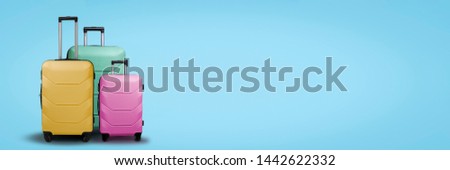 Three multi-colored plastic suitcases on wheels on a blue background. Travel concept, vacation trip, visit to relatives. Banner