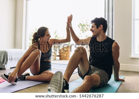Couple giving each other high five after a successful workout together. Man and woman in sports wear doing workout in living room. Royalty-Free Stock Photo #1442676287