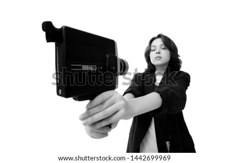 Beautiful girl brunette in a jacket and jeans on a white background shoots selfies of an old vintage movie camera in super 8 format, in isolation