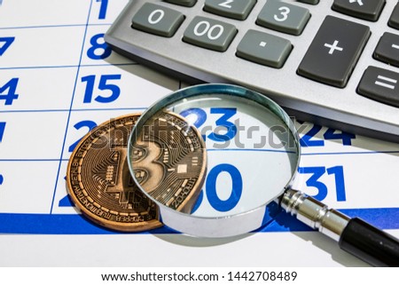 cyripto money mining. close up physical bitcoin coin with calender, hand magnifier and calculator.