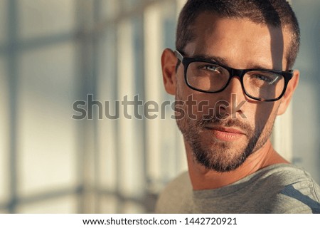 Portrait of stylish young man wearing eyeglasses at home. Closeup face of handsome guy with spectacles with sunlight and shadow reflection on face. Satisfied cool man looking at camera with copy space Royalty-Free Stock Photo #1442720921