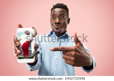 Portrait of man showing screen of mobile phone isolated over coral background. Male model using smartphone for betting, watching sport translations. Creative collage made of 2 people.