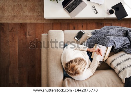 Overhead Shot Looking Down On Woman Working As Social Media Influencer At Home Lying On Sofa Royalty-Free Stock Photo #1442875778