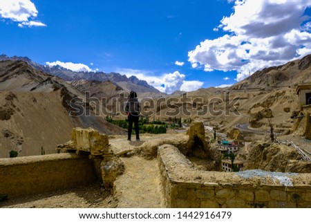 Unidentified female tourist with dark jacket stands on the ruin building at Lamayuru monastery with the mountain range and blue sky in background,Leh,Ladakh,Jammu and Kashmir,India 