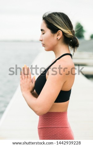 young girl meditating outdoors on the pier by the lake.