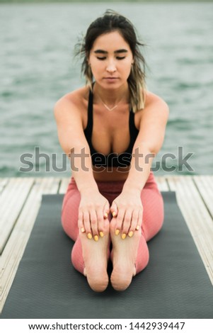 young asian girl doing yoga outdoors on the pier by the lake.