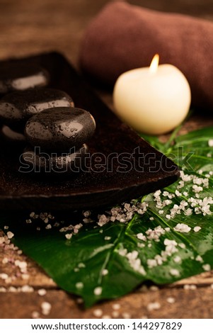 Spa composition of hot stones, a green leaf and a white candle.